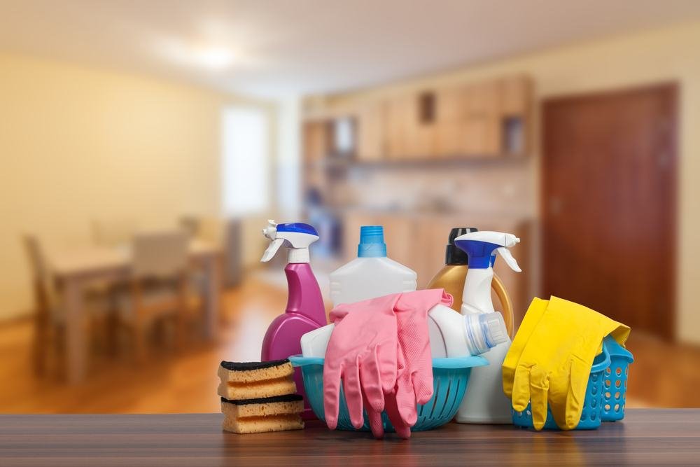 Household cleaning supplies and protective gloves neatly set out on a wooden floor inside a home.