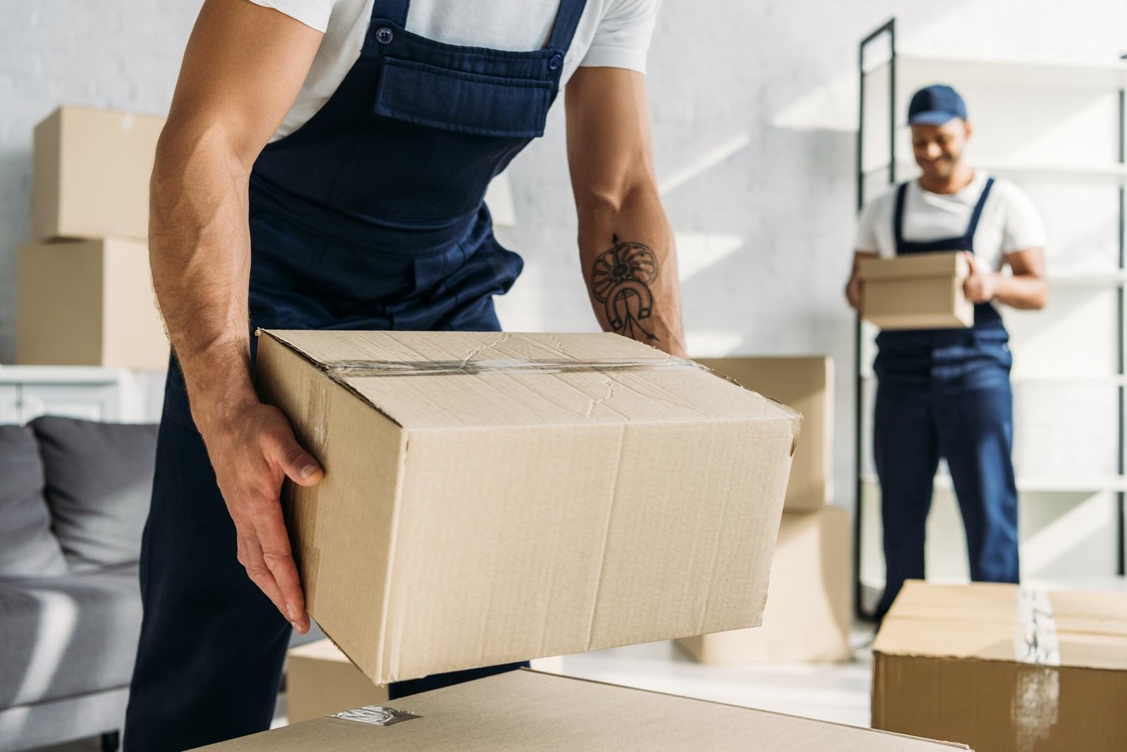 Two uniformed service professionals carrying boxes through a customer's home.