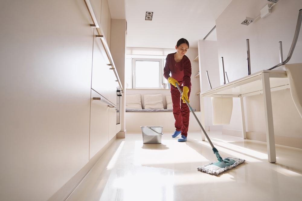 A cleaning professional mopping the floor of a bright kitchen.
